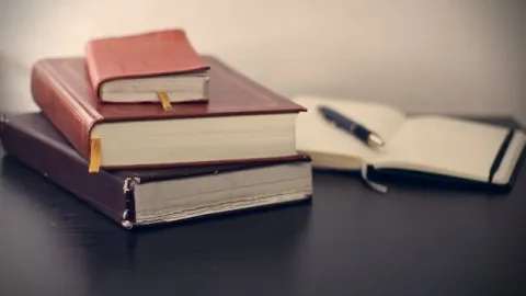 stack of books on a table next to a notebook and a pen